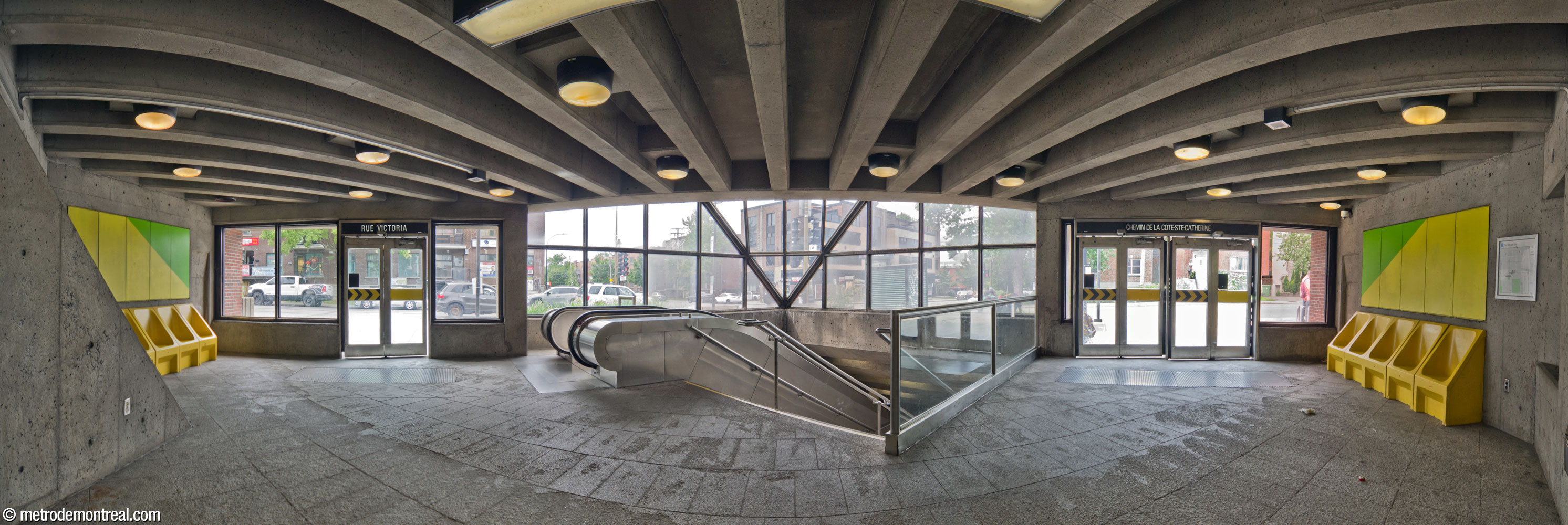 Panorama of the interior of the headhouse, looking along its axis of symmetry and facing the stairs and the broad window above them. The exits on Chemin de la Côte-Sainte-Catherine (right) and Avenue Victoria (left) are positioned symmetrically east and south of the stairwell. Benches in the same style as those on the platforms are surmounted by more brightly coloured murals by the station's architect.