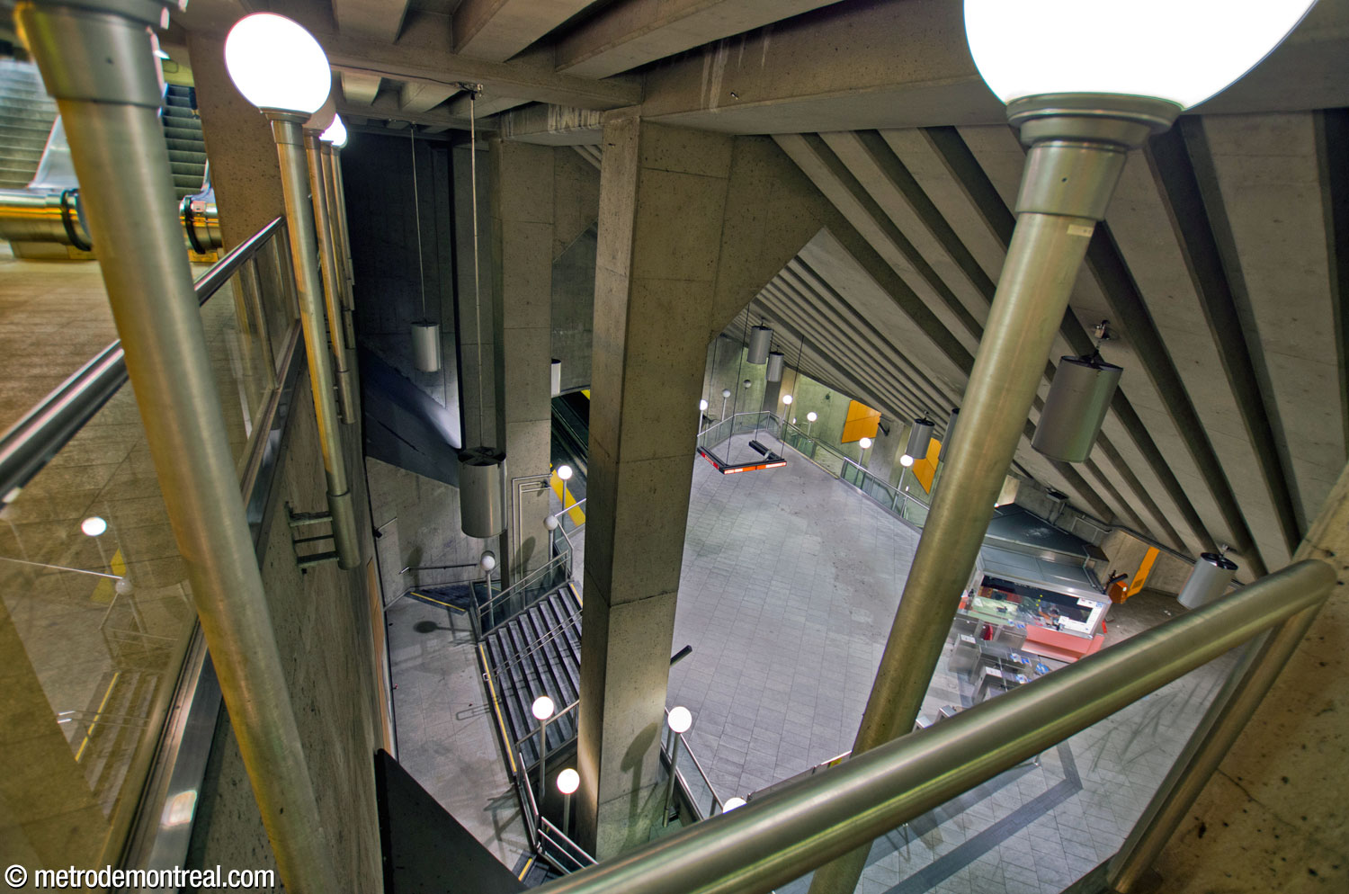 View down from the walkway above the main volume, showing the columns supporting the station roof; below, the staircases to the Côte-Vertu platform curl around them.