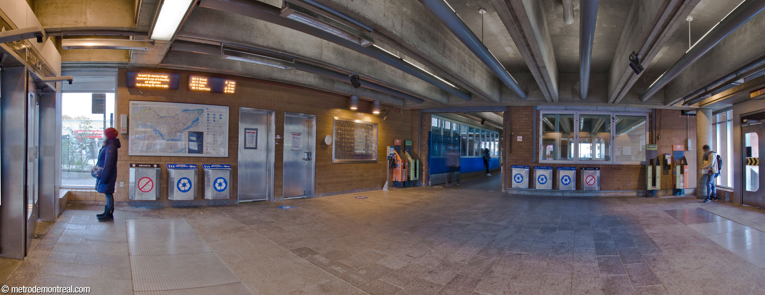 Interior of the bus waiting area on the north side of the Côte-Vertu Nord headhouse. The glassed-in area at right is the main volume over the escalators to the platforms, projecting up to its clerestory window; the walkway at centre-right is in fact a bridge crossing through the volume. Éric Lamontagne's artwork L'Homo urbanus is on the wall at centre, left of the walkway.