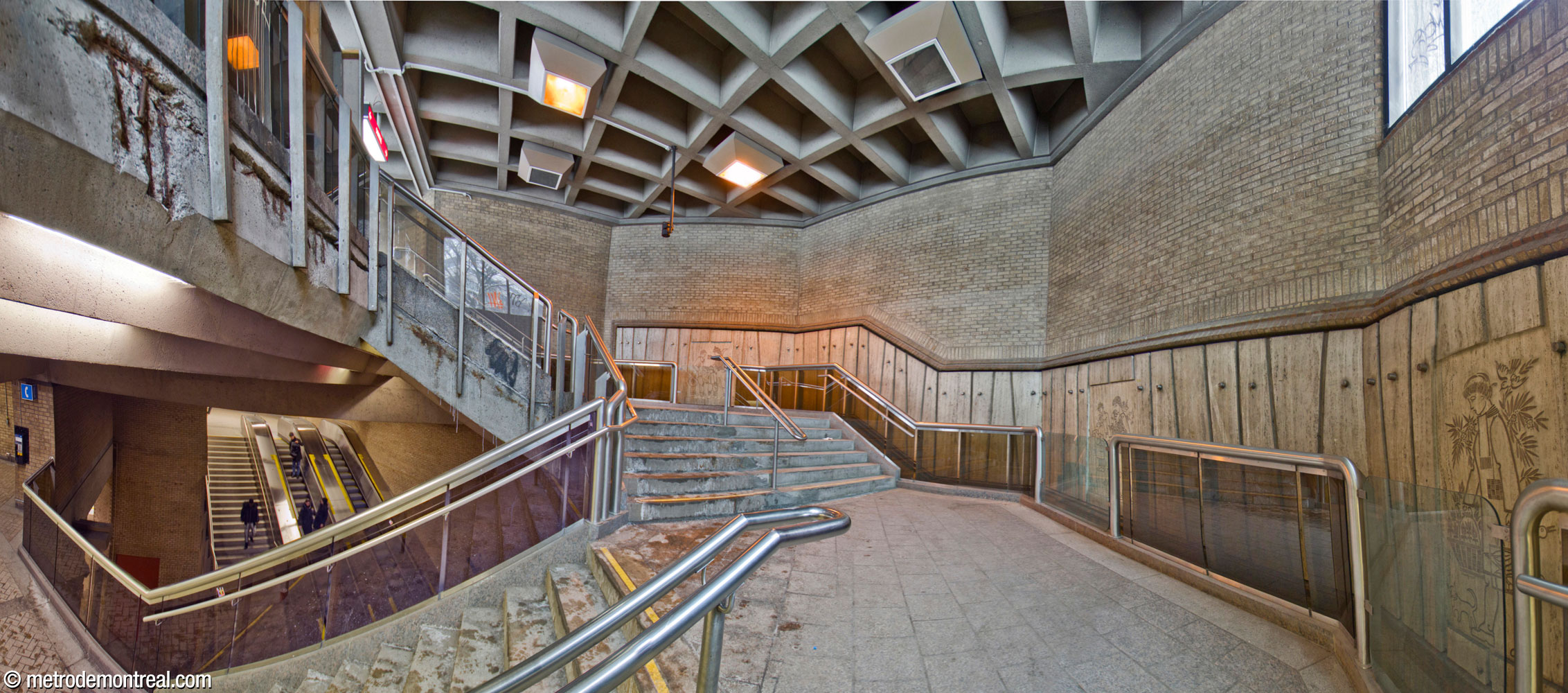 The U-shaped staircase leading down from the Saint-Laurent Ouest headhouse to the ticket hall. The footprint of the headhouse follows the contour of the staircase. At left, the staircase and the ticket hall mezzanine overlook the stairwell down to the Saint-Michel platform.