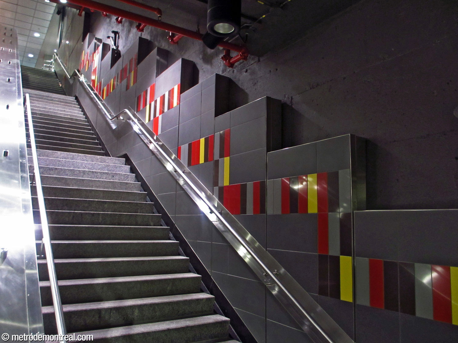 Le mur de la cage d'escalier montant vers la salle de contrôle de l'accès Guy, avec sa bande composée de carreaux multicolores.