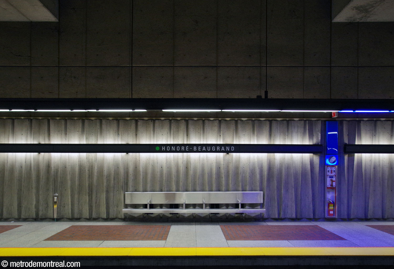 The concrete frieze along the platform walls, dramatically emphasized by the backlit nameplates.