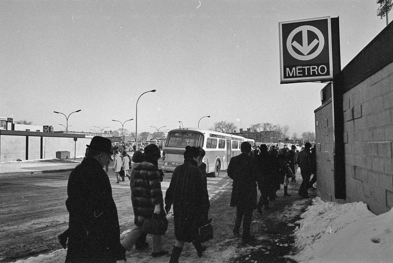 Passengers wait beside the south bus terminal entrance; the north one is also seen at left.