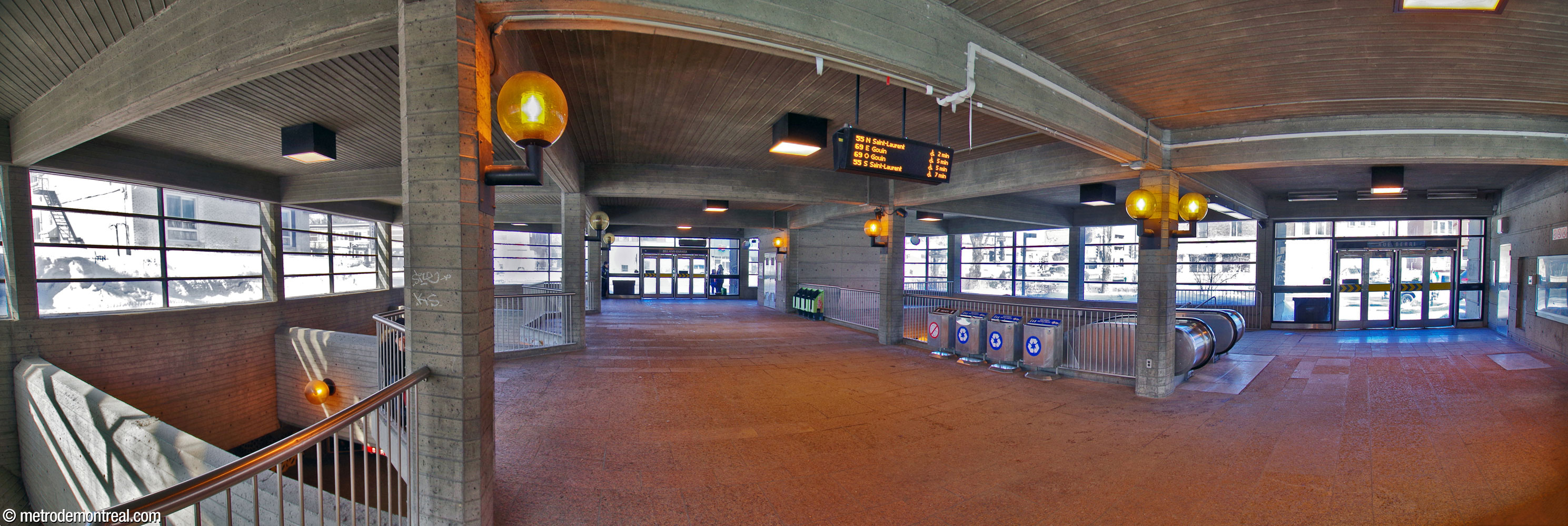 Panorama of the interior of the Berri headhouse, whose exterior walls are almost entirely glazed. Entrances are at centre (Boulevard Henri-Bourassa) and right (Rue Berri). At left, the western edge of the building is largely open to the ticket hall below, admitting sunlight. Natural light also enters via the stairwell to the ticket hall, at centre-right.