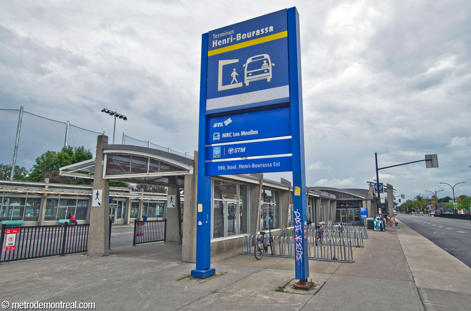 The street side of the north building of the bus terminal. Doors on the main part of the building serve passengers arriving on foot or on non-terminating buses running on the street. At left, a partially enclosed marquee shelters passengers alighting from buses in the bus loop as they make their way toward the entrance.