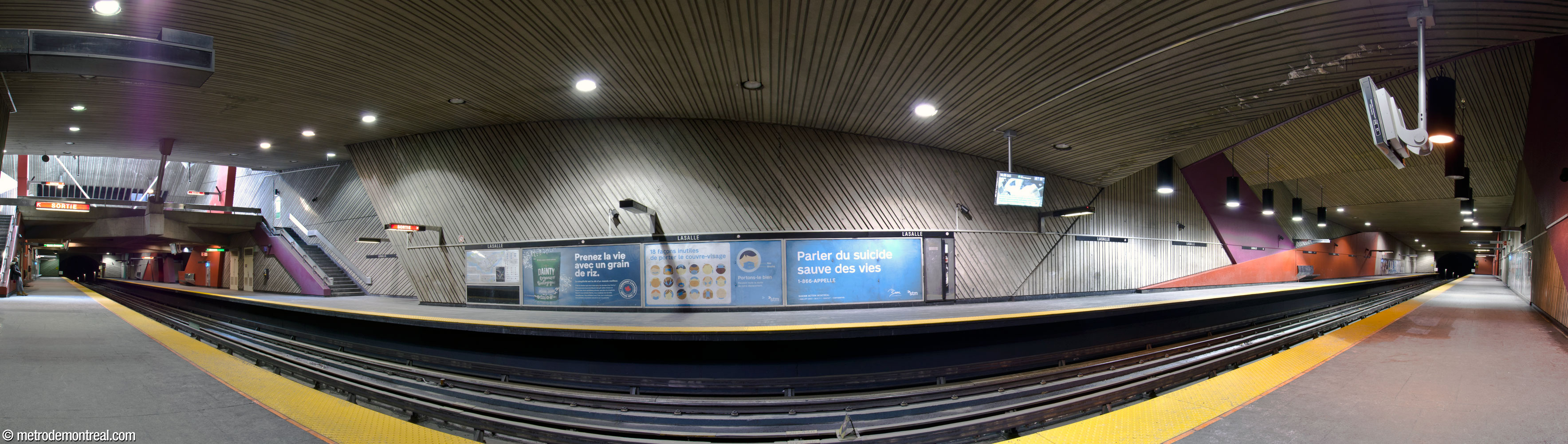 Panorama des quais de la station depuis le quai Honoré-Beaugrand. On voit les murs irréguliers, le béton cannelé, les grandes formes colorées et la mezzanine ensoleillée (gauche).