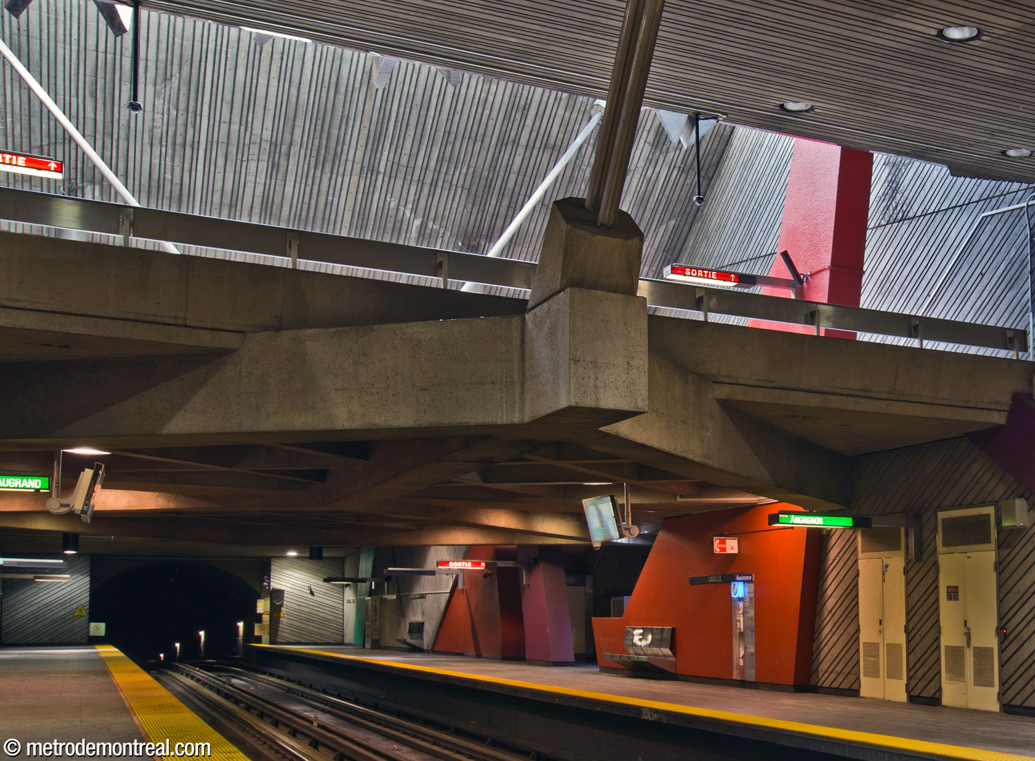 La mezzanine surplombant la moitié ouest des quais. Une forme rouge transperce le plancher de la mezzanine. On note la charpente en béton qui soutient la mezzanine et qui est suspendue du plafond par des tiges métalliques.