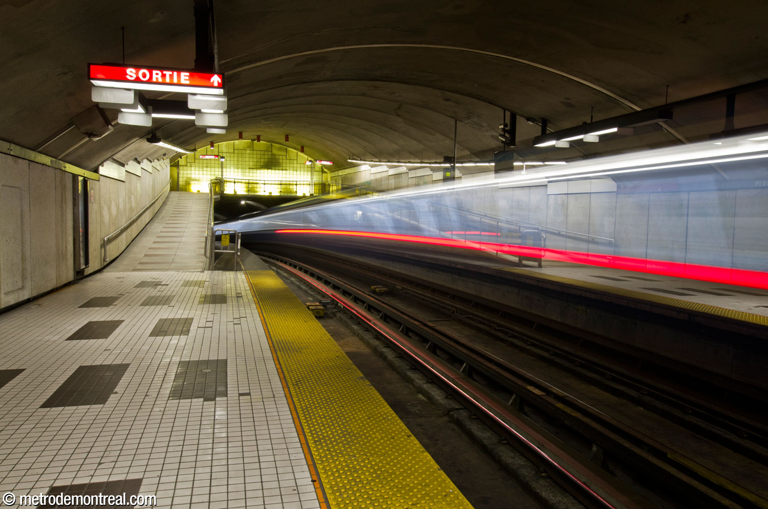 Les lumières d'un train quittant la station tracent la forme des voies, qui entament une courbe à même la nef de la station.