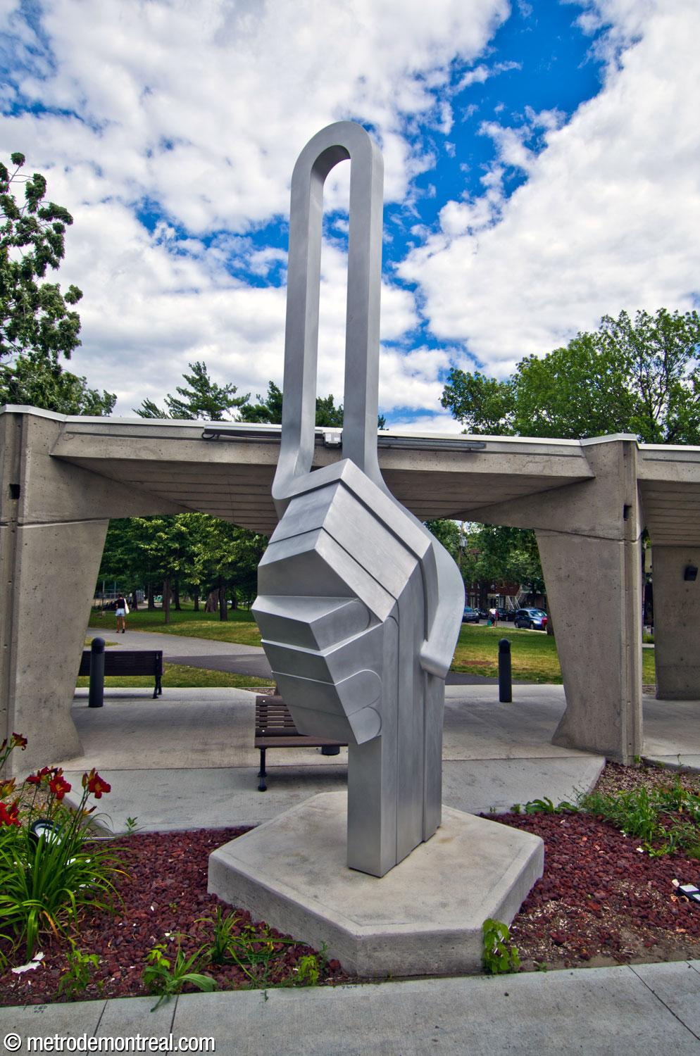 La sculpture Relier de Catherine Sylvain, présentant la forme d'une poignée de main combinée avec une boucle qui suggère un trajet de métro. Elle se situe dans un lit de fleurs adjacent à l'édicule de l'ascenseur.