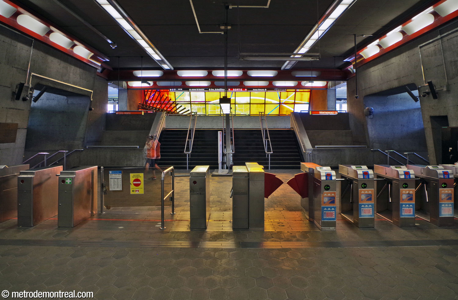 Les tourniquets de la billetterie. L'escalier ajouté en 2015 raccorde la zone de contrôle à la passerelle afin d'en faire deux sorties supplémentaires. Au fond, le vitrail et la sculpture de Marcelle Ferron illuminent l'espace.