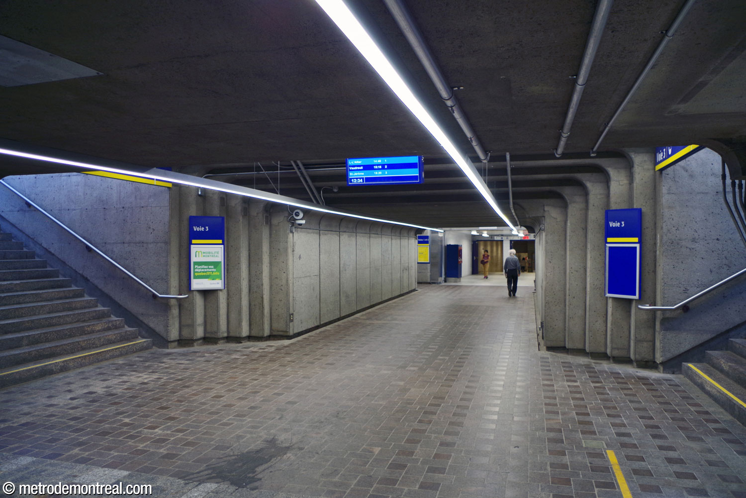 Le tunnel reliant la billetterie originelle à la gare de trains de banlieue. Les escaliers de part et d'autre mènent vers les édicules d'accès sur les deux quais. Au fond, le tunnel se poursuit vers l'édicule sur le campus du CUSM et vers l'accès intérieur à l'hôpital via le stationnement souterrain.
