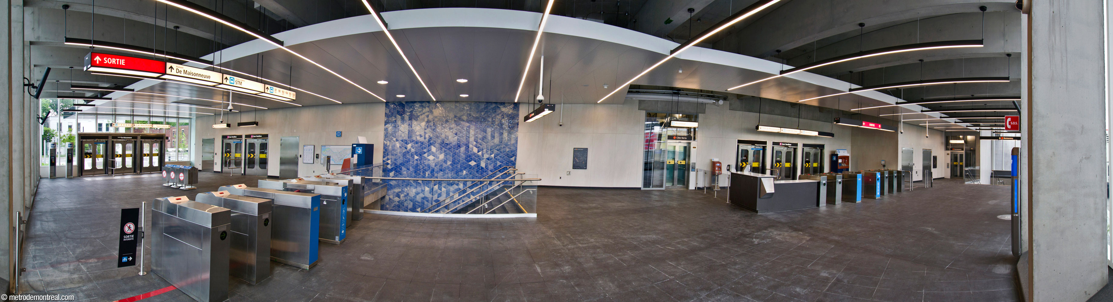 L'intérieur de la section ouest du nouvel édicule, offrant un accès sans préposé au métro. Les tourniquets à droite mènent à l'accès à la gare et au CUSM. À centre-gauche, le premier volet du cycle de murales de Patrick Bernatchez surplombe l'escalier vers le quai Côte-Vertu. L'ascenseur et escalier à droite donnent accès au quai Montmorency.