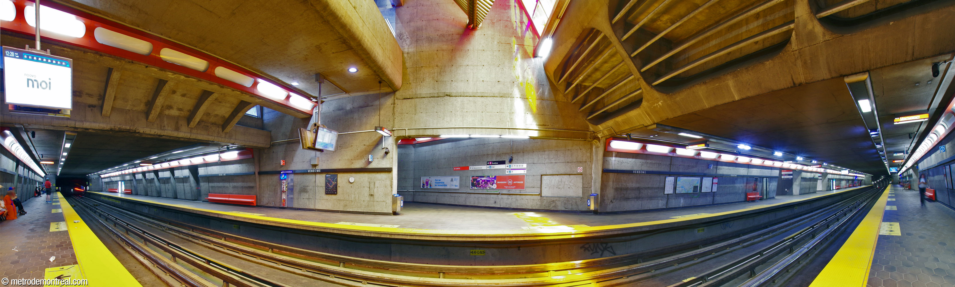 Panorama des quais depuis le quai Montmorency. Les murs sont de béton apparent, assortis de bancs et de châssis de luminaires rouge orange. Au centre, le volume principal de la station à l'intérieur de l'édicule originel et l’escalier vers la salle de contrôle dans cet édicule. Dans le volume, le vitrail et la sculpture de Marcelle Ferron surplombent les voies, faisant jaillir de la lumière teinte de couleurs brillantes. Les accès au nouvel édicule se trouvent plus loin sur les quais, à droite.