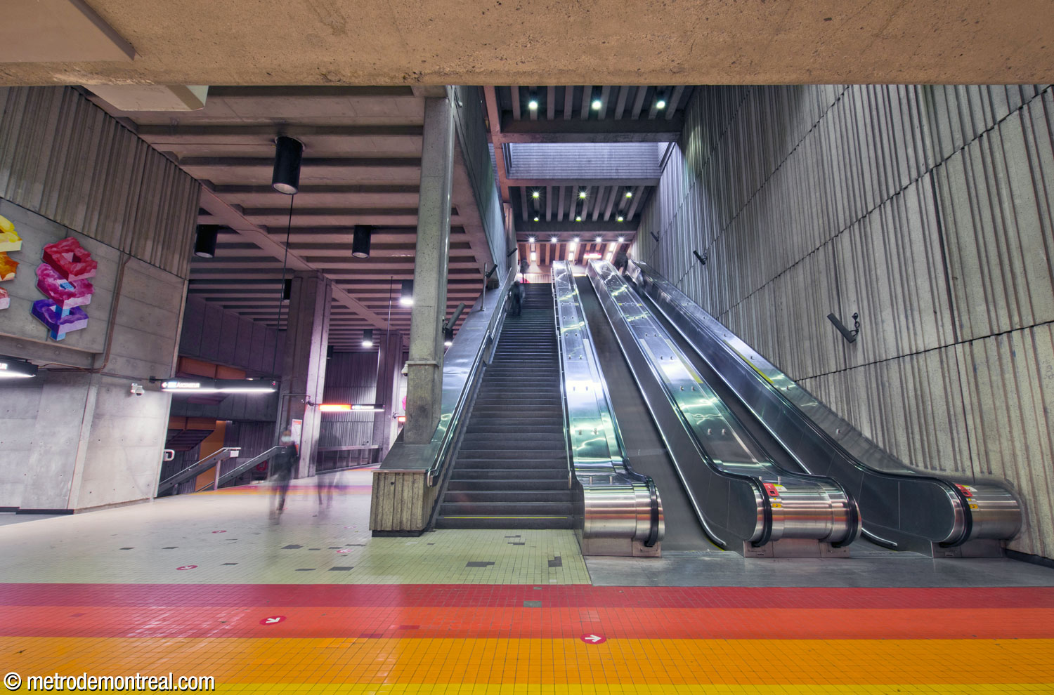 The main stairwell seen from below, looking up to ticket hall level. The transept and access to platform level is at left. One of Marianne Chevalier's mural sculptures is visible above the elevator entrance at far left.